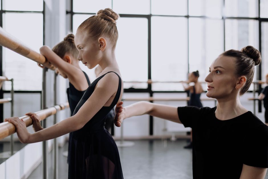 A young ballerina practices ballet with guidance from her instructor in a dance studio.