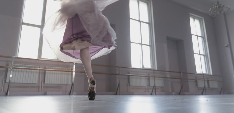 A close-up shot of a ballerina performing an elegant turn in a bright ballet studio.