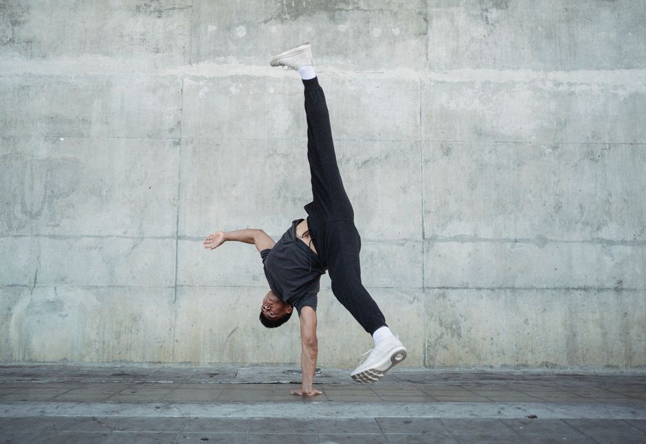 Flexible male dancer in sportswear and white sneakers doing handstand during break dance on urban street